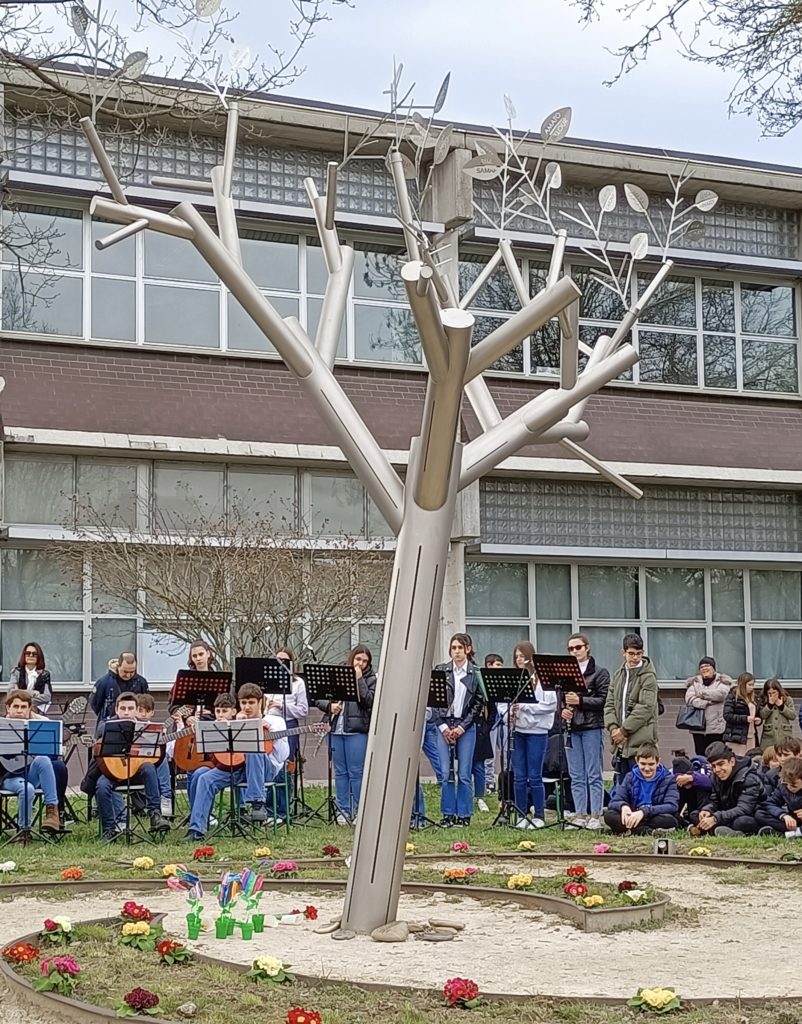 Studenti suonano strumenti musicali davanti a una scultura metallica di un albero